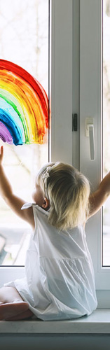 Little girl finger painting rainbow on window